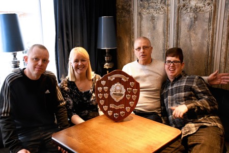 Four people sat around a shield award.