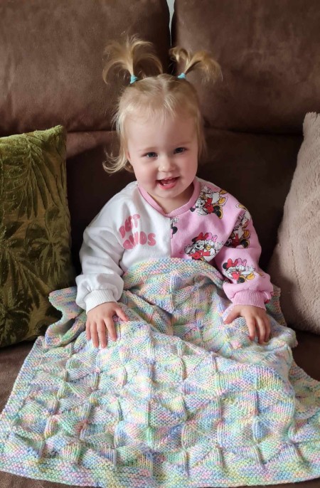 Little girl sat with a multi-coloured blanket on her lap.