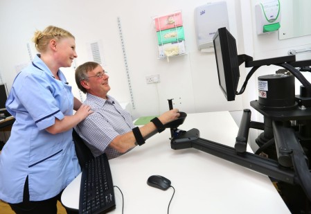 A member of staff supporting a patient with their hand movements on a computer.