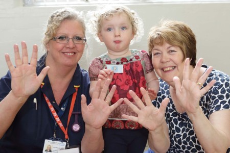 Infection control nurse Susan Besbrode and grandmother Elizabeth Hogg with little Millie holding up their hands