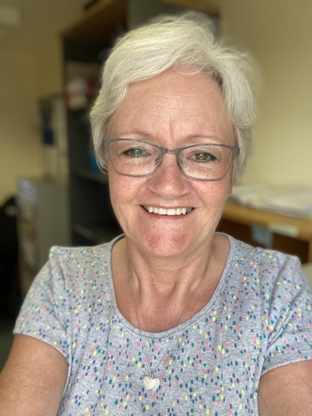 A woman with grey hair and glasses, smiling.