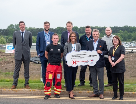 A group of people standing in front of a construction site smiling and holding a charity donation cheque.