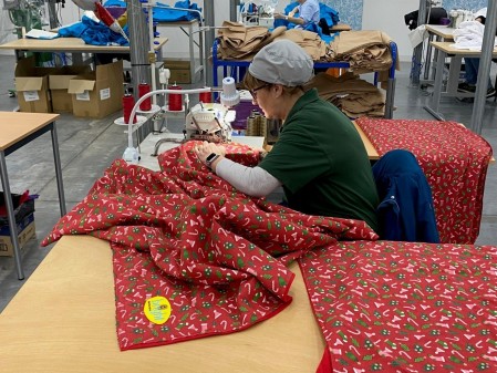 A woman using a sewing machine to put together a Christmas blanket.