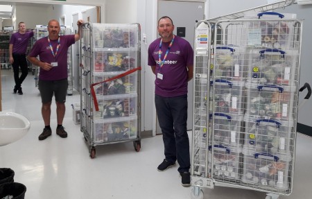 Three men standing next to some crates. The crates are stacked full of boxes of food.