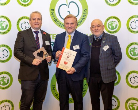 A photograph of three men. Two of them are holding awards.