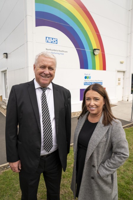 A portrait of a man and a woman. There is a rainbow painted on the wall behind them.