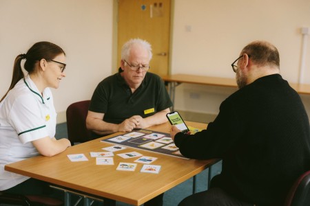 A photograph of three people sat around a table playing a game with cards
