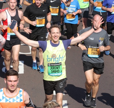 A crowd of people running. A man in the middle is smiling and is holding his arms up.