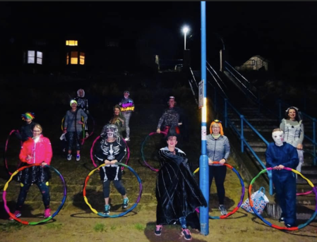 A group of people in fancy dress holding hula hoops. It's night time.