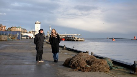 A man and a woman standing either side by a fish harbour 