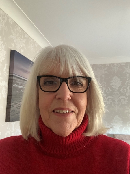 Lady with grey hair wearing glasses smiling to the camera 