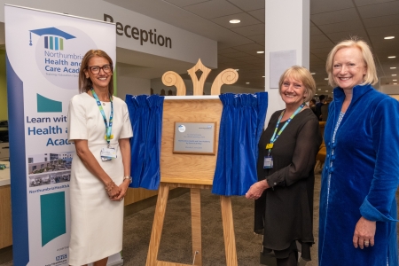 3 people stood with a plaque that has been unveiled from behind curtains.