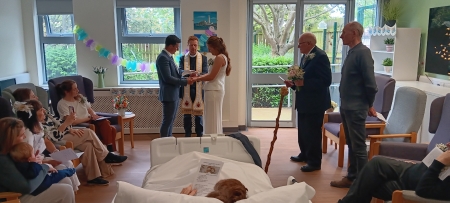 Man and woman standing in front of hospital chaplain receiving a wedding blessing with their family surrounding them. 