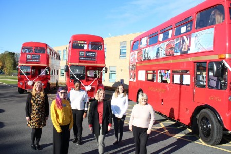 A photograph of a group of women standing in front of three red busses.