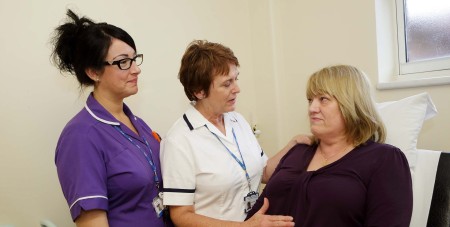 A female patient sat on an exam chair talking to two nurses