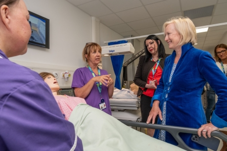People stood around a hospital bed with a manikin in it.