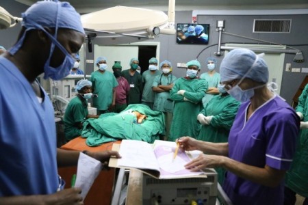 A group of people in an operating theatre wearing scrubs getting prepared to operate.