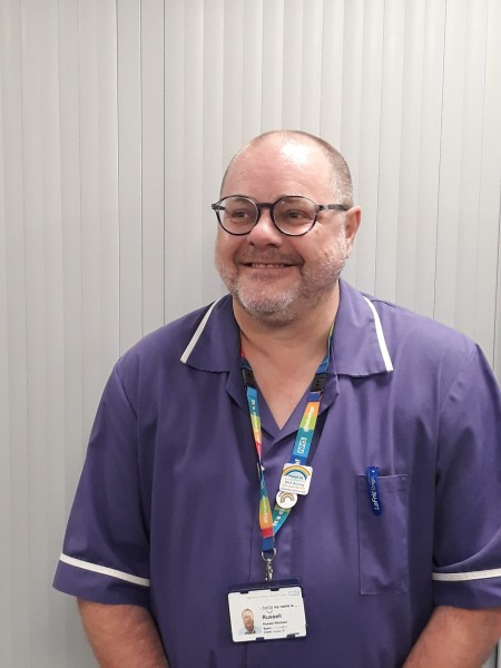 A man wearing glasses and a purple uniform, smiling.