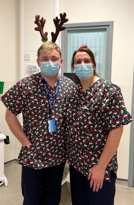 Man and woman wearing christmas themed scrubs and facemasks standing close together 