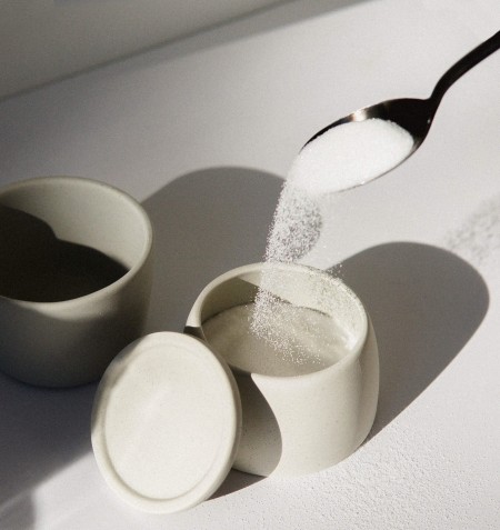 A spoon pouring sugar into a jar.