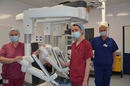 Three women standing next to some robotic equipment.