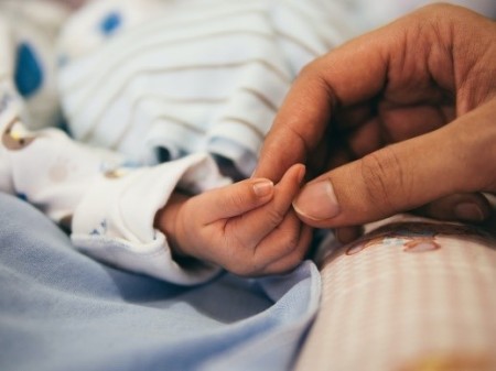 A close-up photograph of a babies hand being held but an adult's hand.