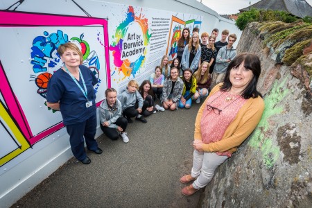 A group of children and two adults standing next to some outdoor artwork.