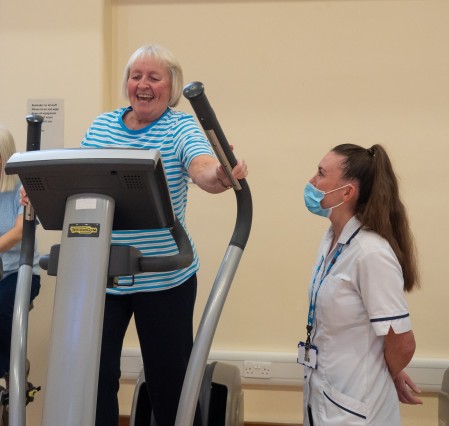 A physio observing an older woman doing exercise on a cross trainer.