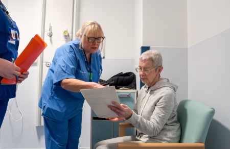 A member of staff talking to a patient while looking at a sheet of paper.
