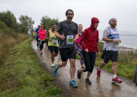 A photograph of lots of people running in the rain. One main is looking at the camera smiling and giving a thumbs up.