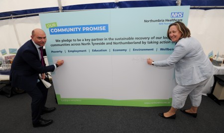 A photograph of a large board labelled 'Our community promise'. There is a man and a woman each side of it signing it.