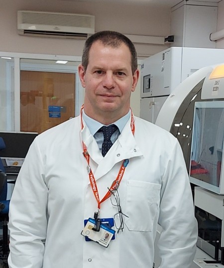 A man with dark hair wearing a lab coat.